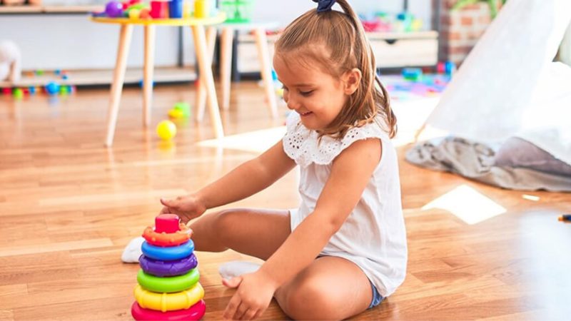 A young child sitting on the floor, absorbed in stacking colourful rings